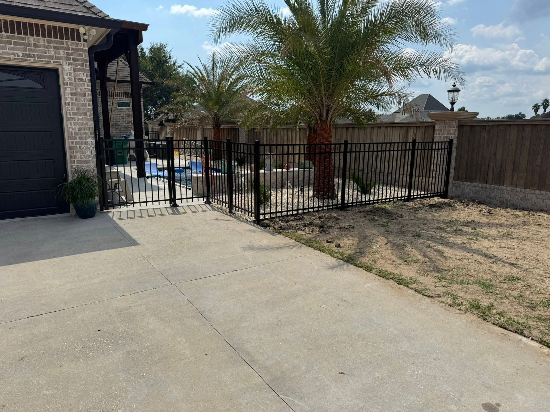 Black metal fence around a yard with palm trees, driveway, and a garage.