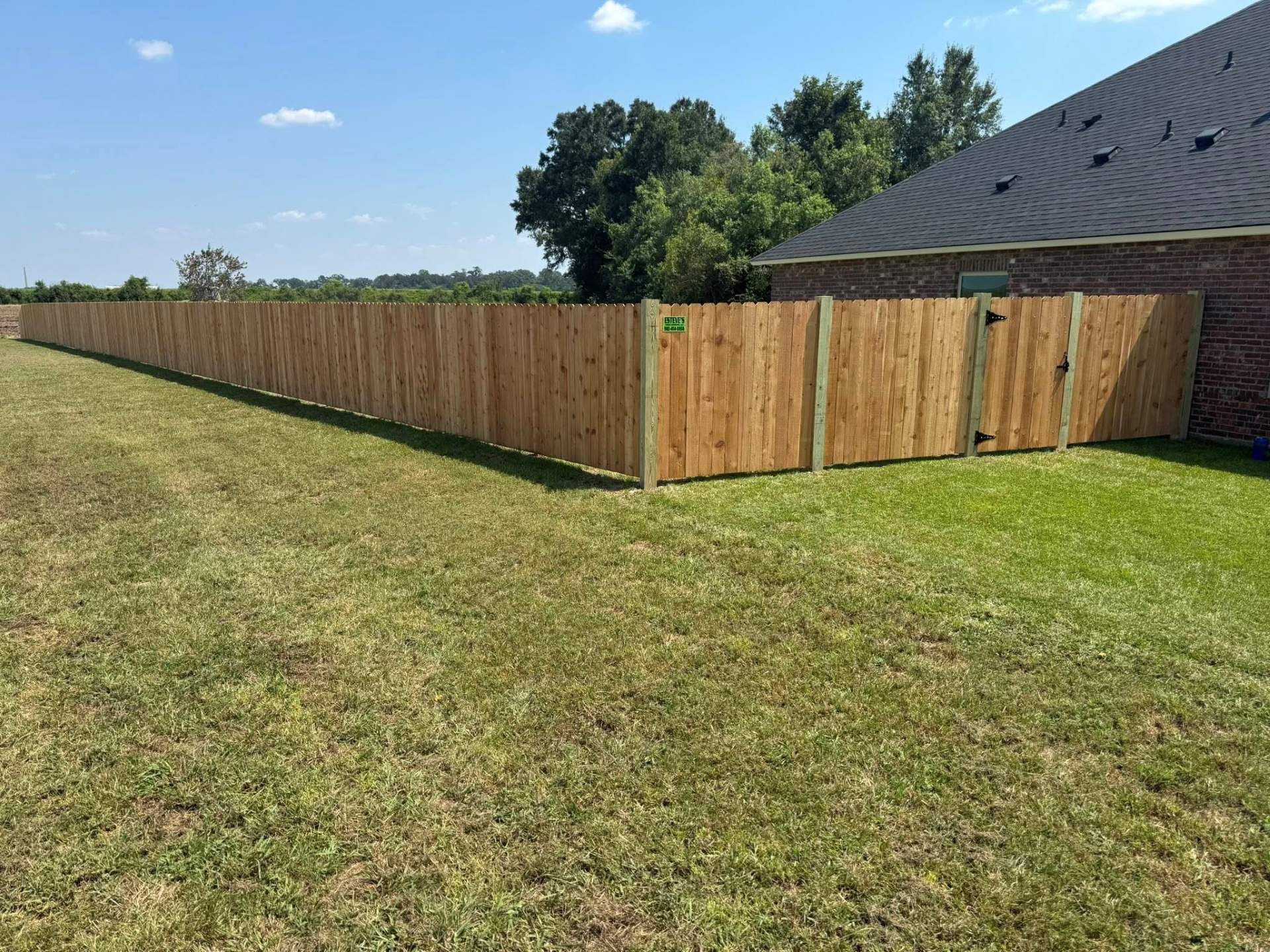 Wooden privacy fence in a grassy yard, with a gate and a house in the background.