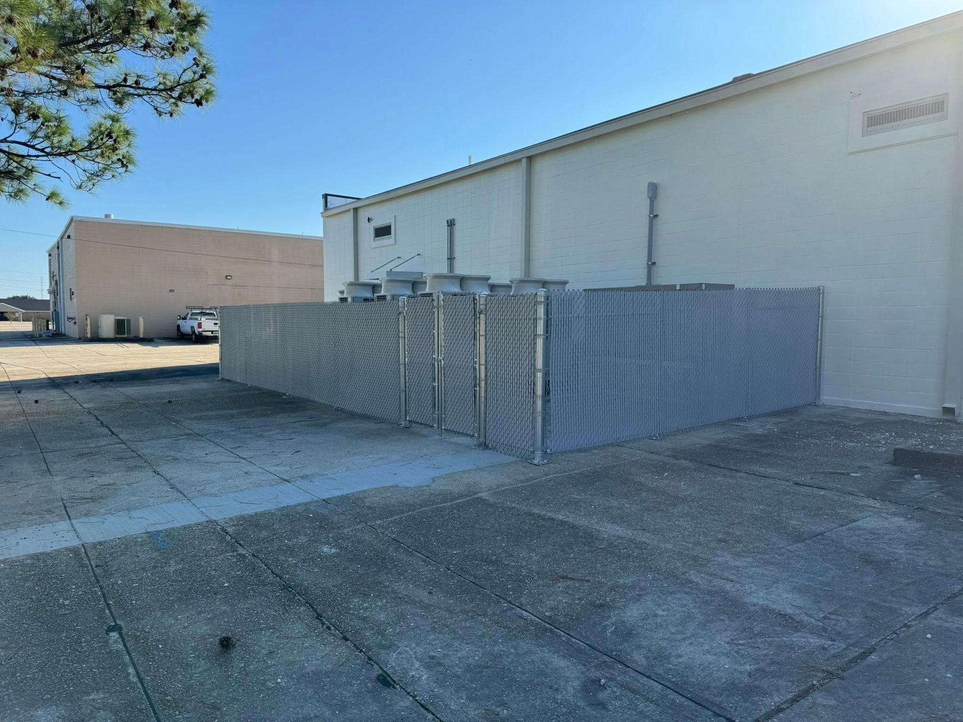 Gray metal fence alongside a white building with several upright metal panels. Bright, sunny day.