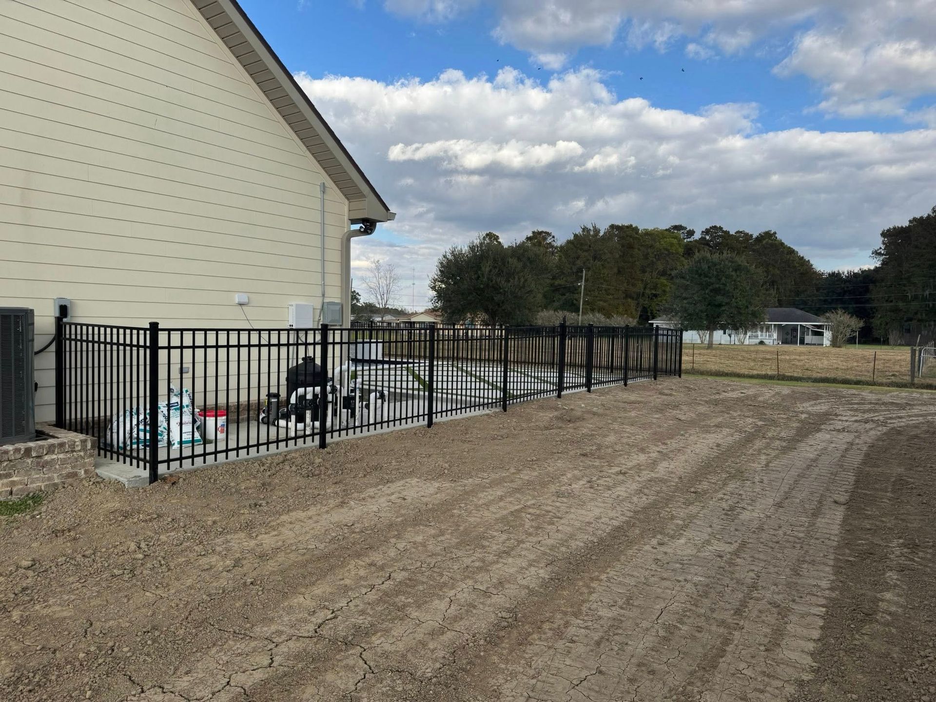 Black metal fence surrounds a gravel yard beside a beige house on a sunny day.