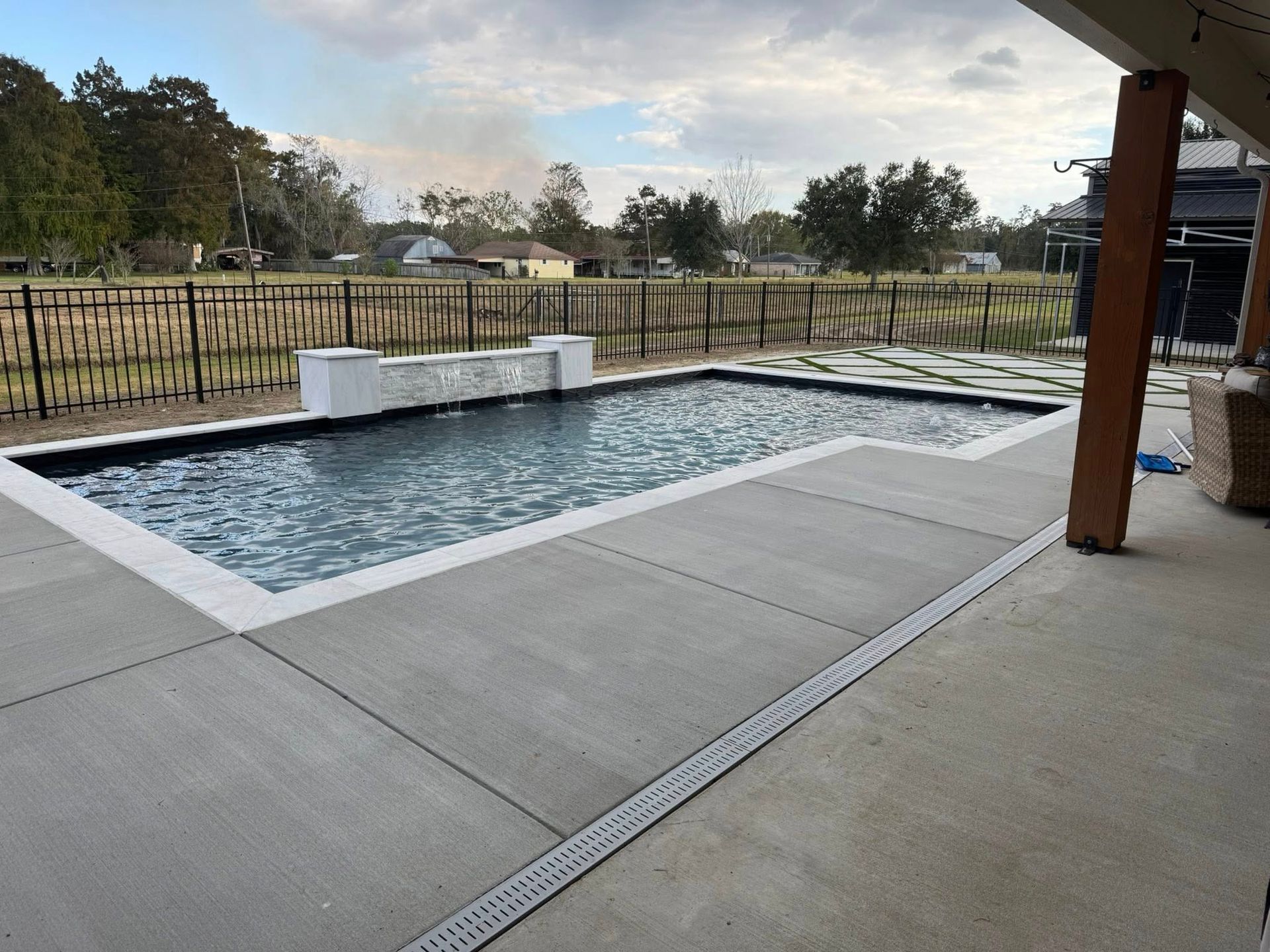 A rectangular swimming pool with a fountain and concrete patio.