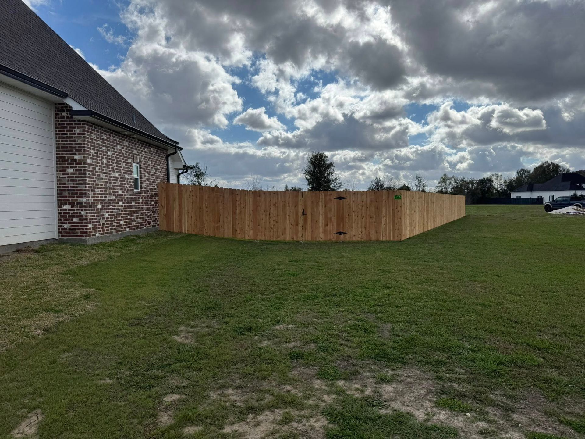 Wooden fence in a grassy yard, next to a brick house under a cloudy sky.