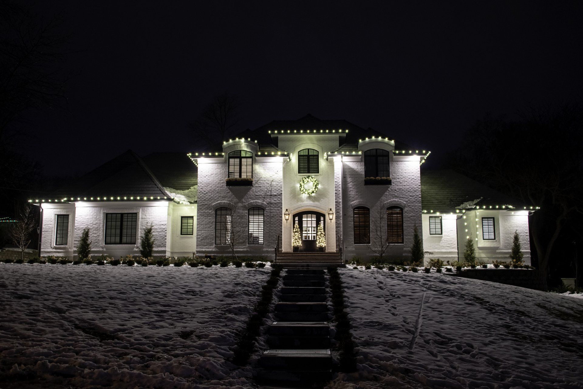 A large white house is lit up at night with christmas lights.