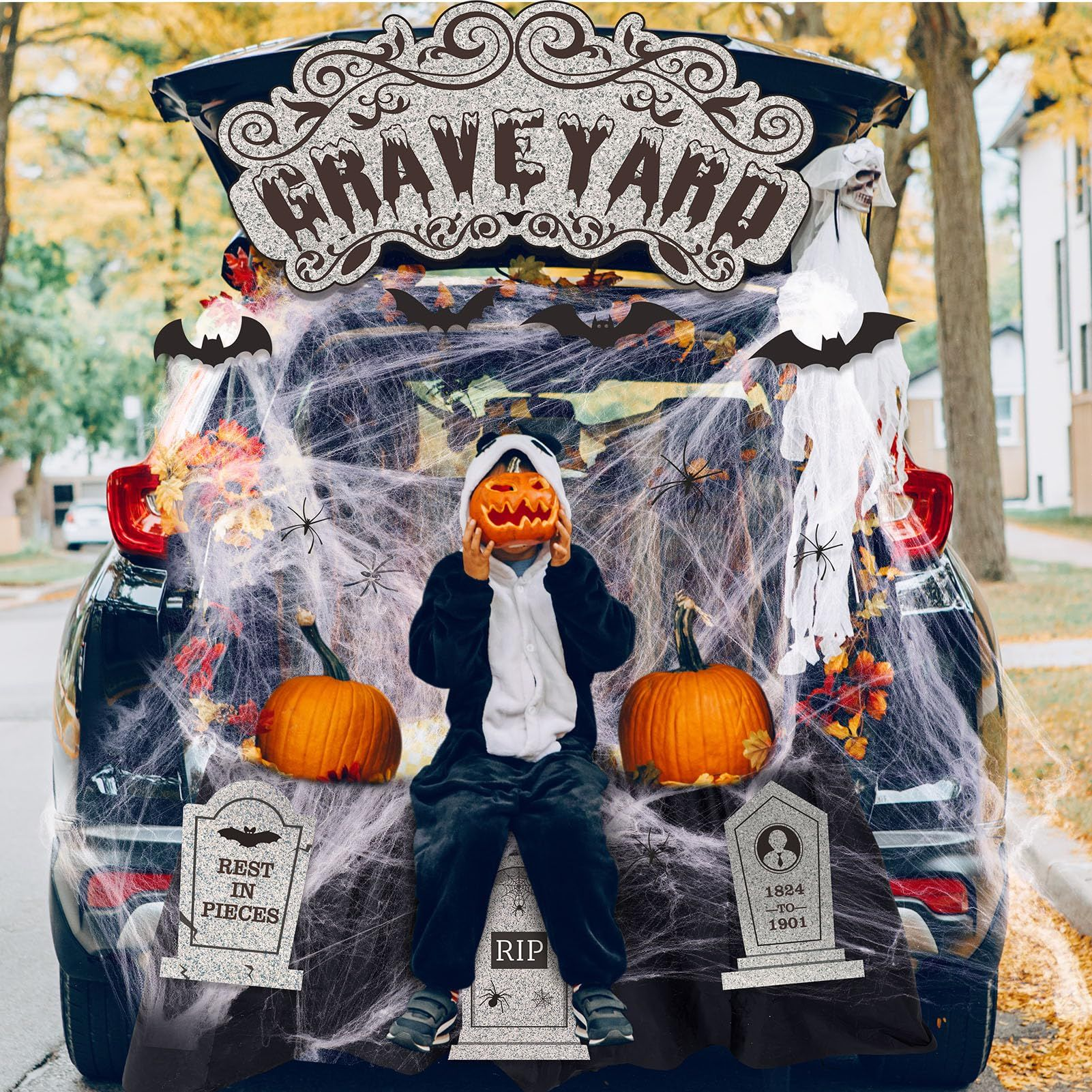 Halloween trunk-or-treat display with child in pumpkin mask. Car trunk decorated as a graveyard with pumpkins and spiderwebs.