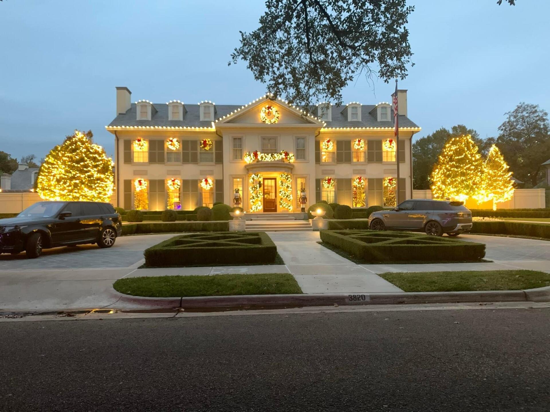 Two cars are parked in front of a large house decorated for christmas