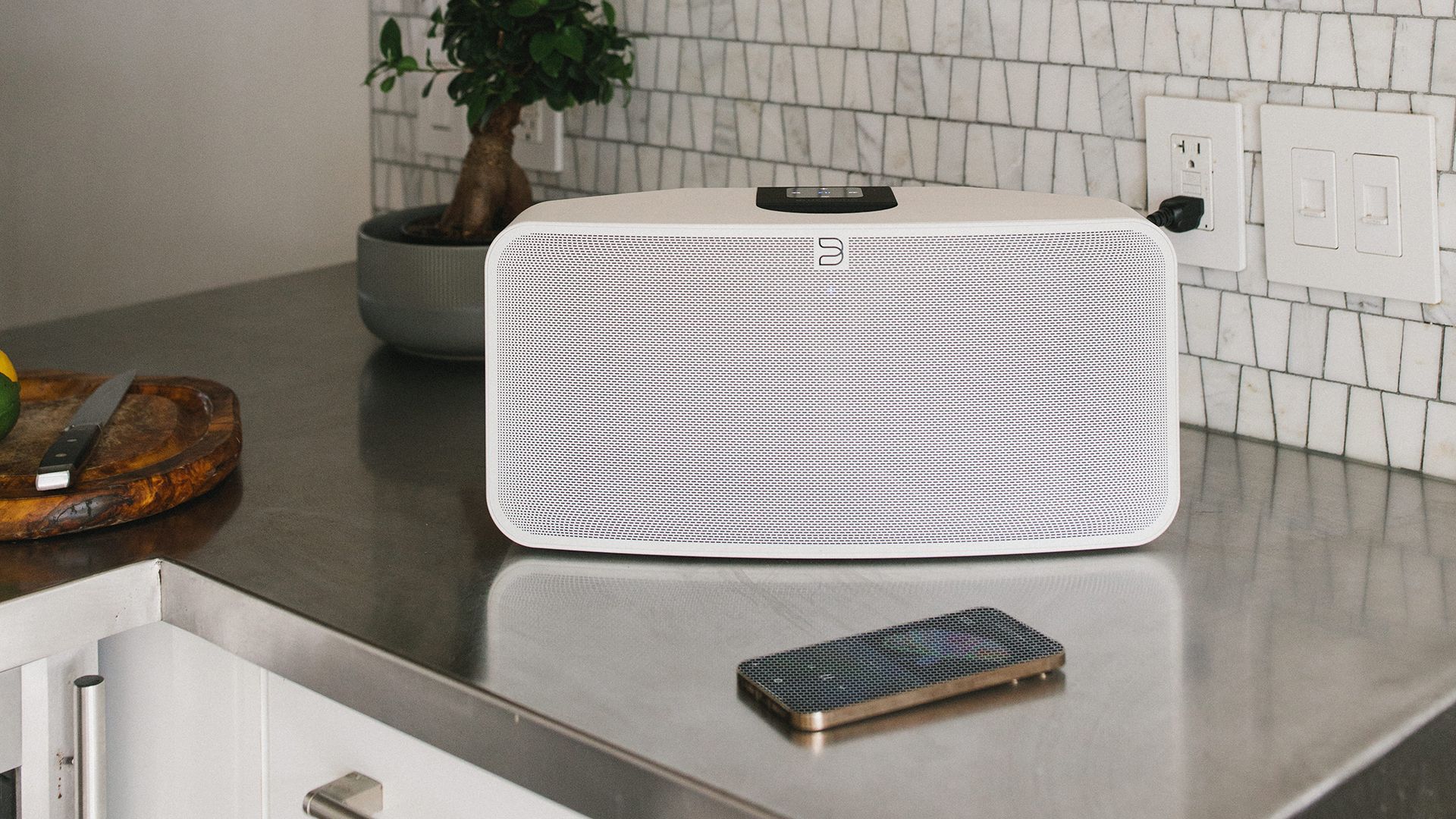 Un haut-parleur blanc est assis sur un comptoir de cuisine à côté d'un téléphone portable.