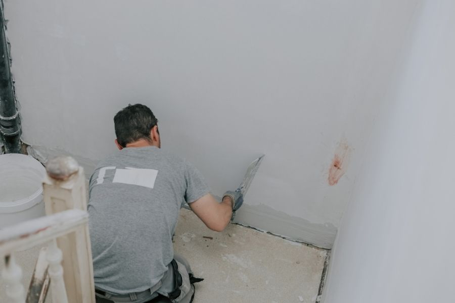 Worker patching and repairing drywall after mold damage in a residential room