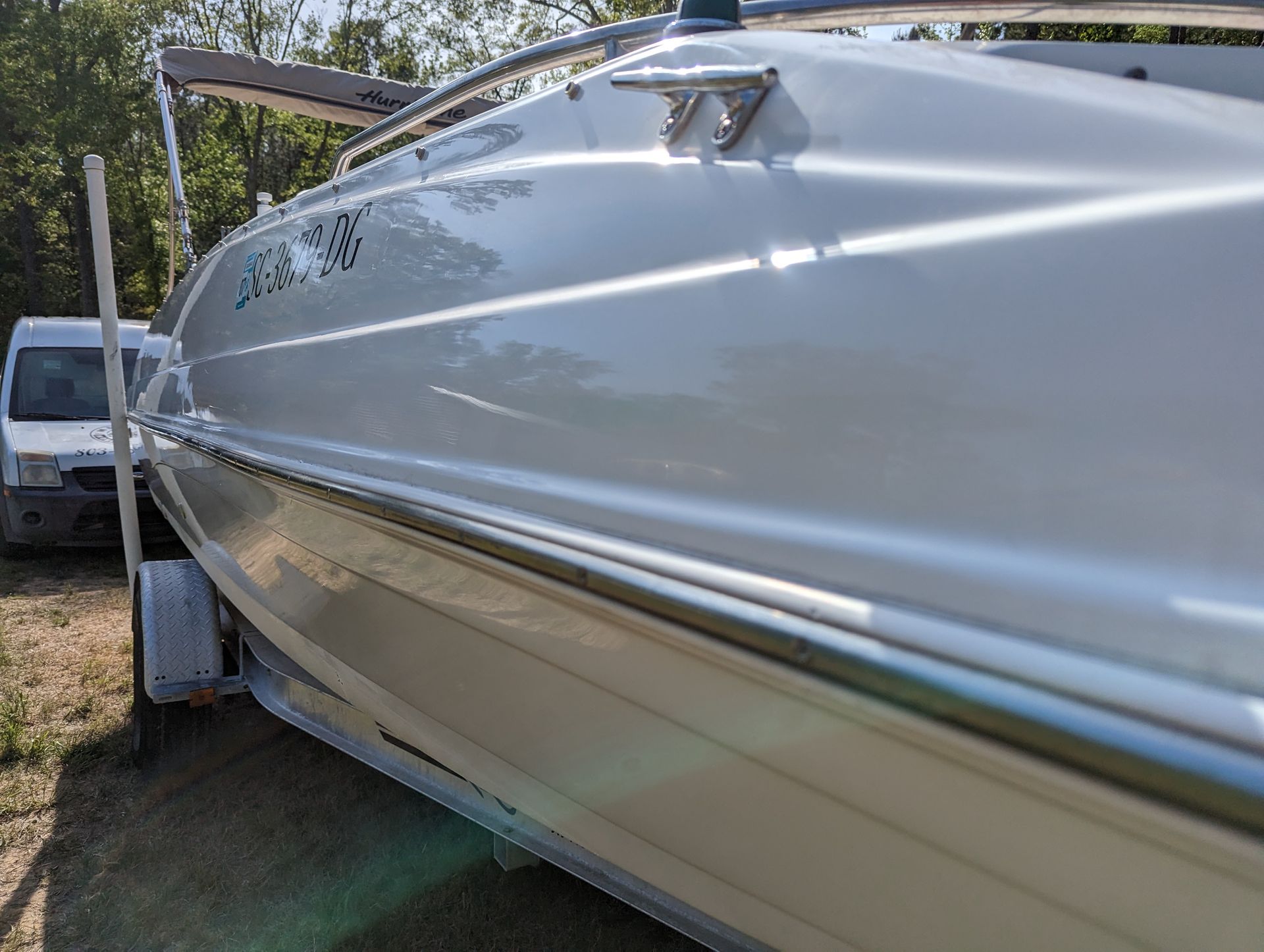 A white boat is parked on a trailer in a field.