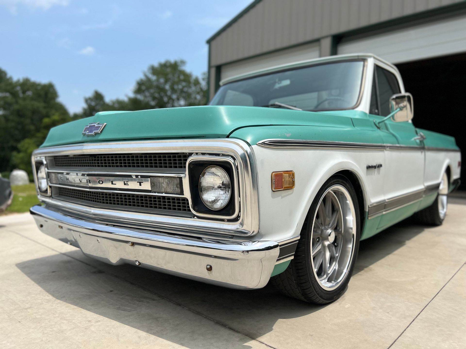 A green and white chevrolet truck is parked in front of a garage.