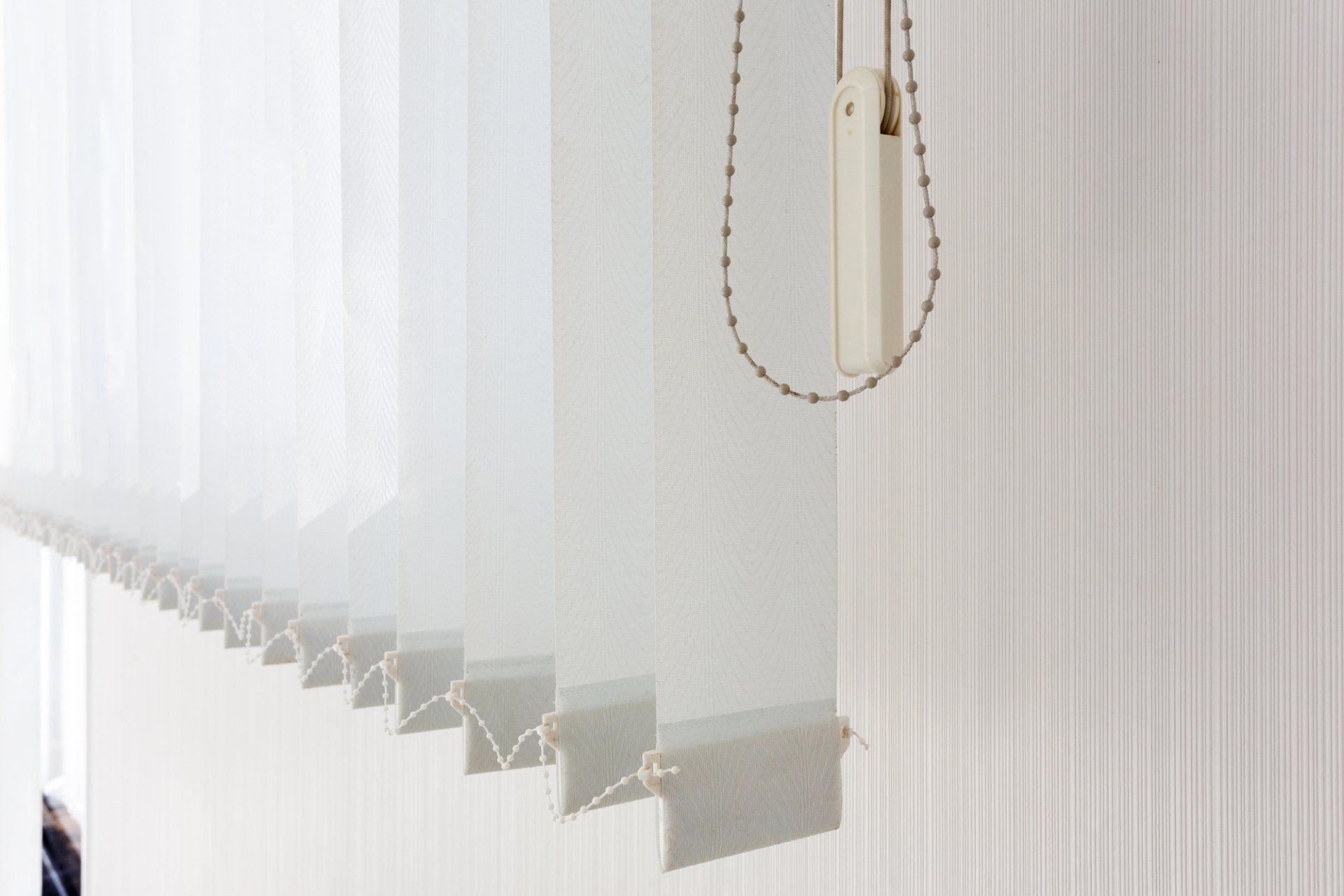 Close up of bottom of white vertical blinds against white wall.