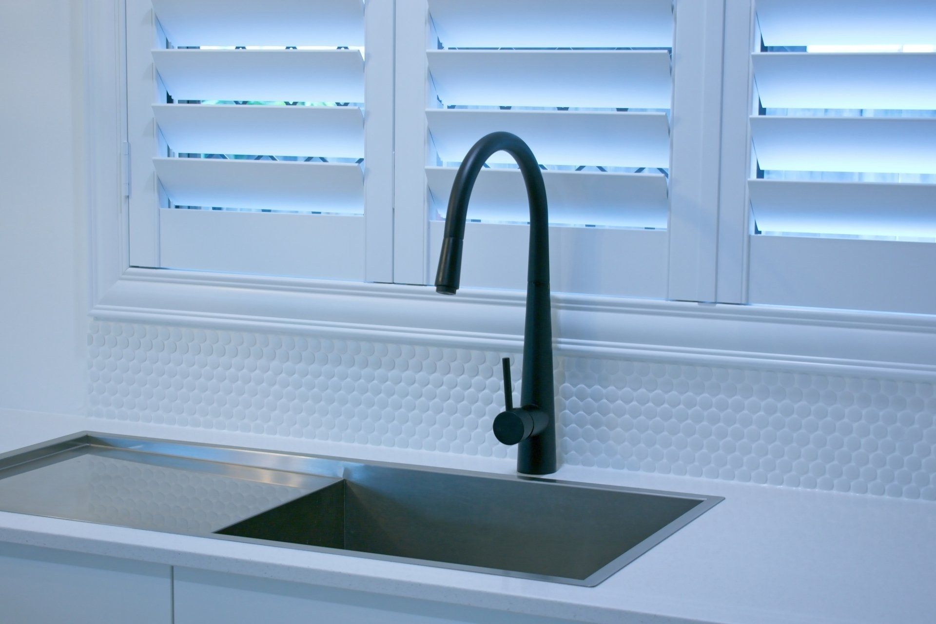 White plantation shutters, opened over kitchen sink and bench, contrasted with black mixer tap.