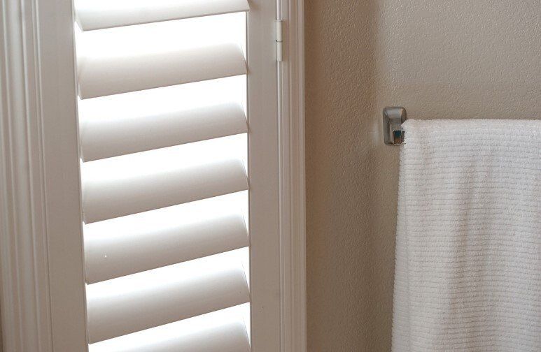 Close up of white plantation shutters, slightly open, with white towel hanging on towel rack.