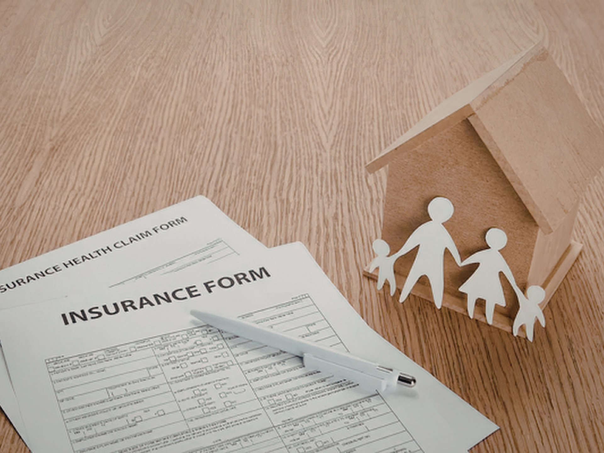 Hands placing a protective roof over a model house with a family and car, representing coverage from a home and auto insurance broker service in San Tan Valley, AZ