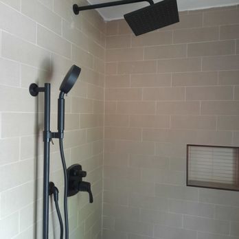 A shower with a black shower head and a brick wall.