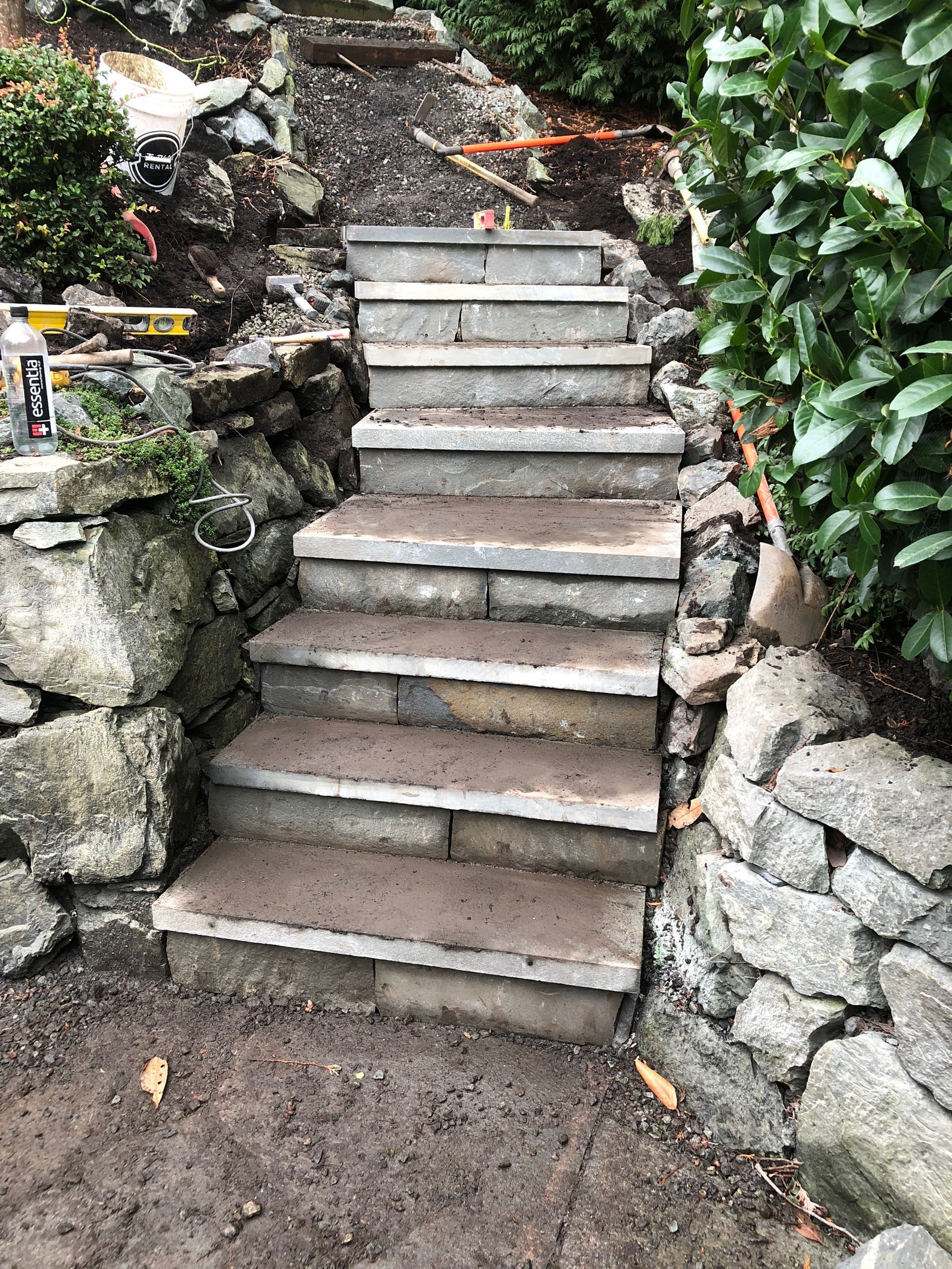 Stone steps built into a hillside, surrounded by rock walls and lush greenery; work by West Coast Landscape & Hardscape. 