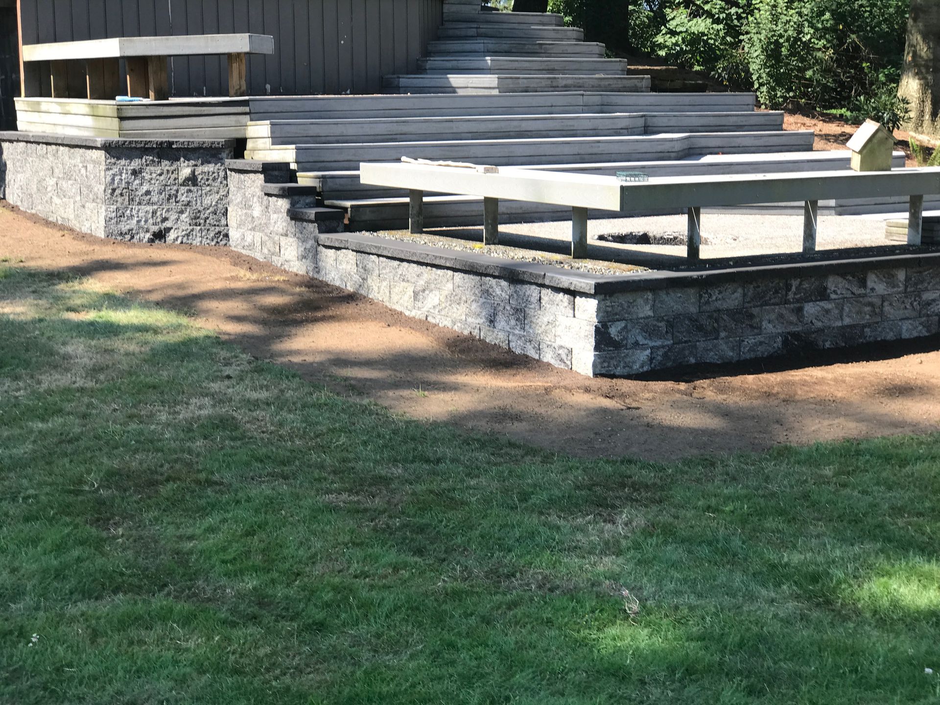 Stone steps and low concrete benches in a grassy outdoor area beside a wooden building.