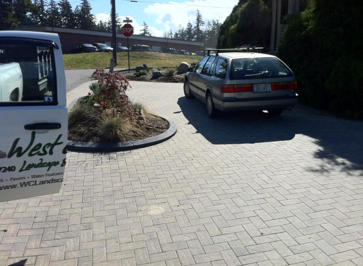A gray station wagon parked on brick pavers; a landscaping truck is open nearby; work by West Coast Landscape & Hardscape. 