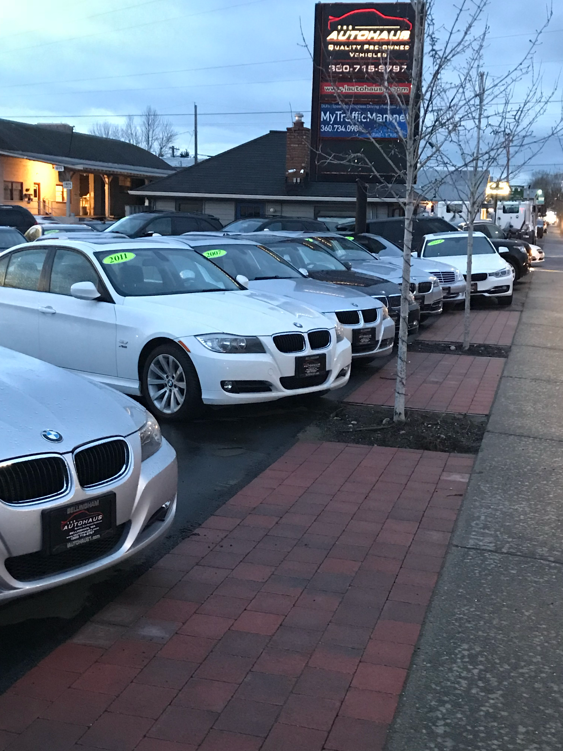 Cars parked in front of a car dealership, a sign above them reads 