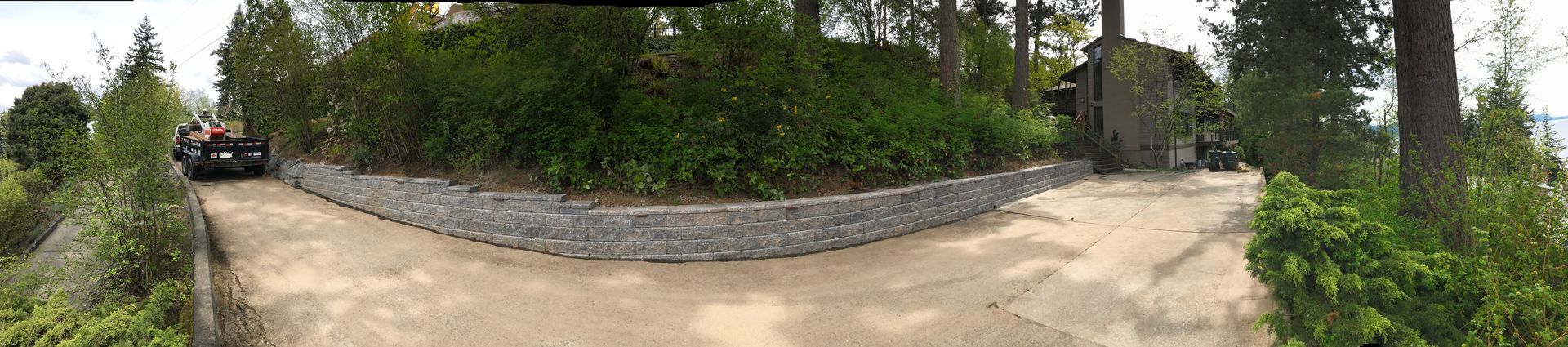 A gravel driveway leads to a stone building surrounded by trees and shrubbery; work by West Coast Landscape & Hardscape. 