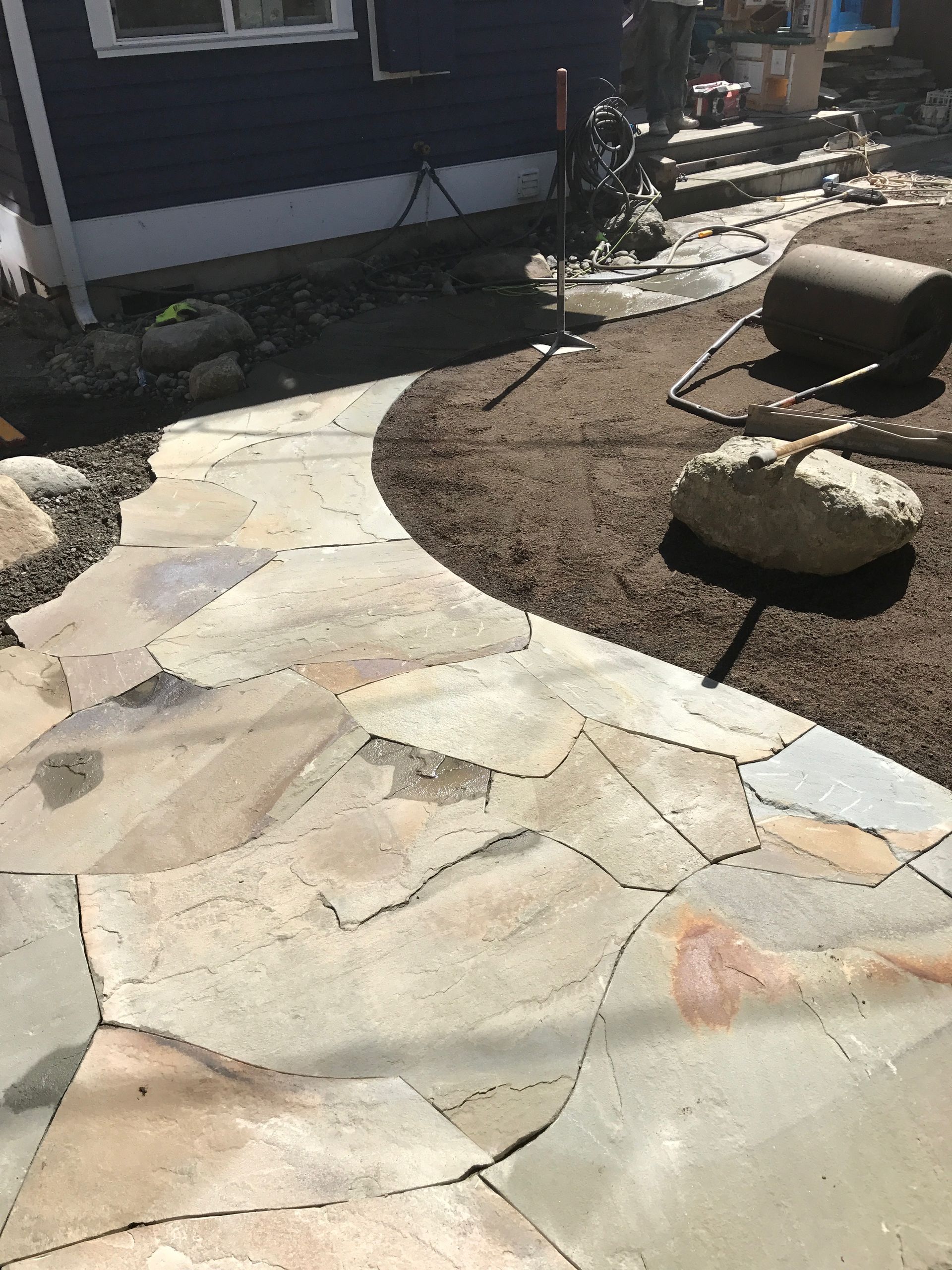 Stone pathway winding through a yard, leading to stairs. Brown mulch borders the path; work by West Coast Landscape & Hardscape. 