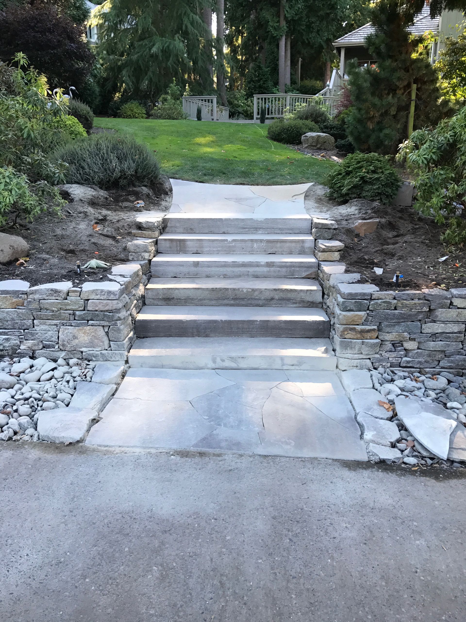 Stone steps leading up a grassy hill, flanked by stone walls and landscaping; work by West Coast Landscape & Hardscape. 