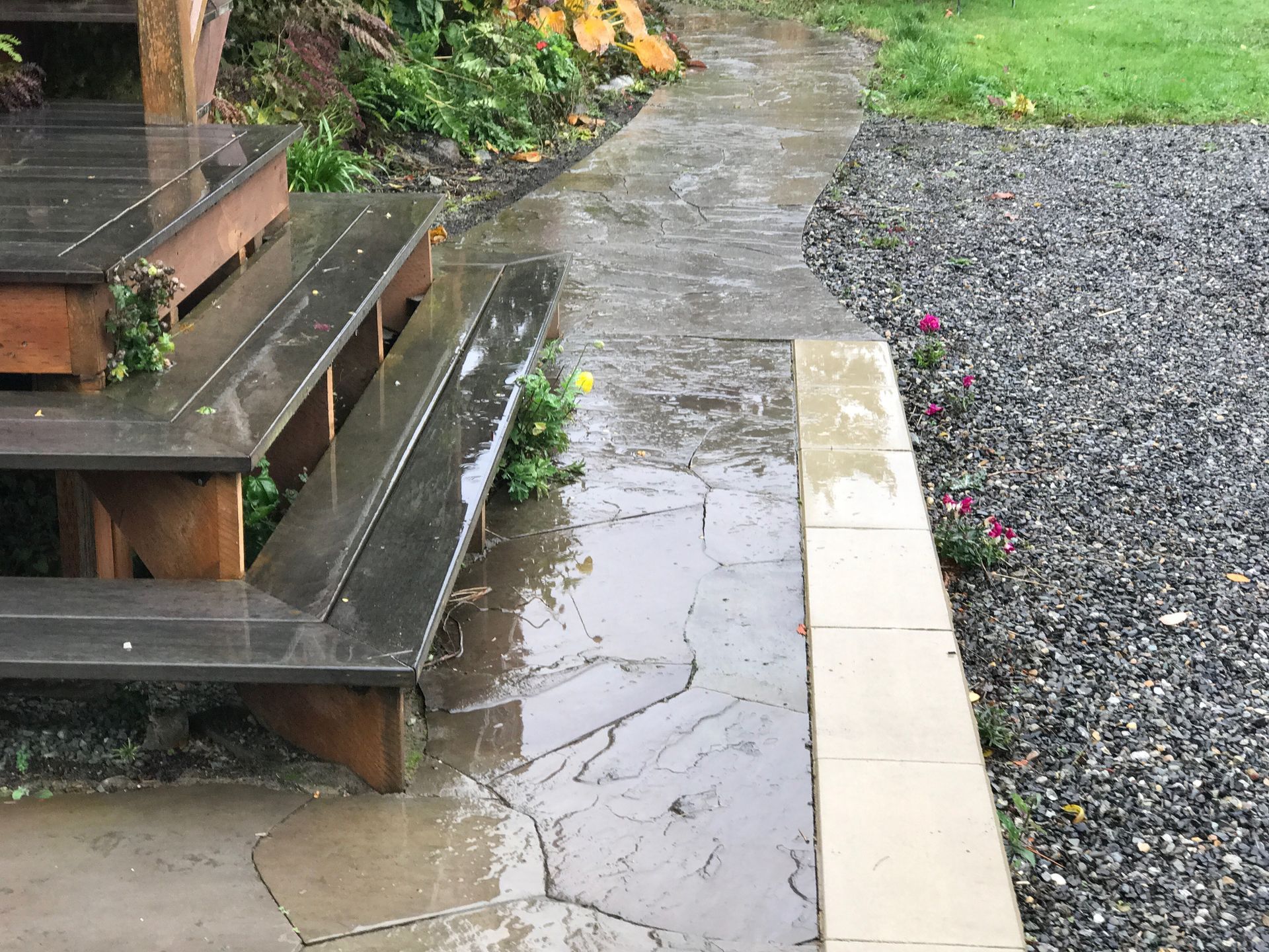 Wet stone patio and steps next to gravel area with pink flowers; work by West Coast Landscape & Hardscape. 