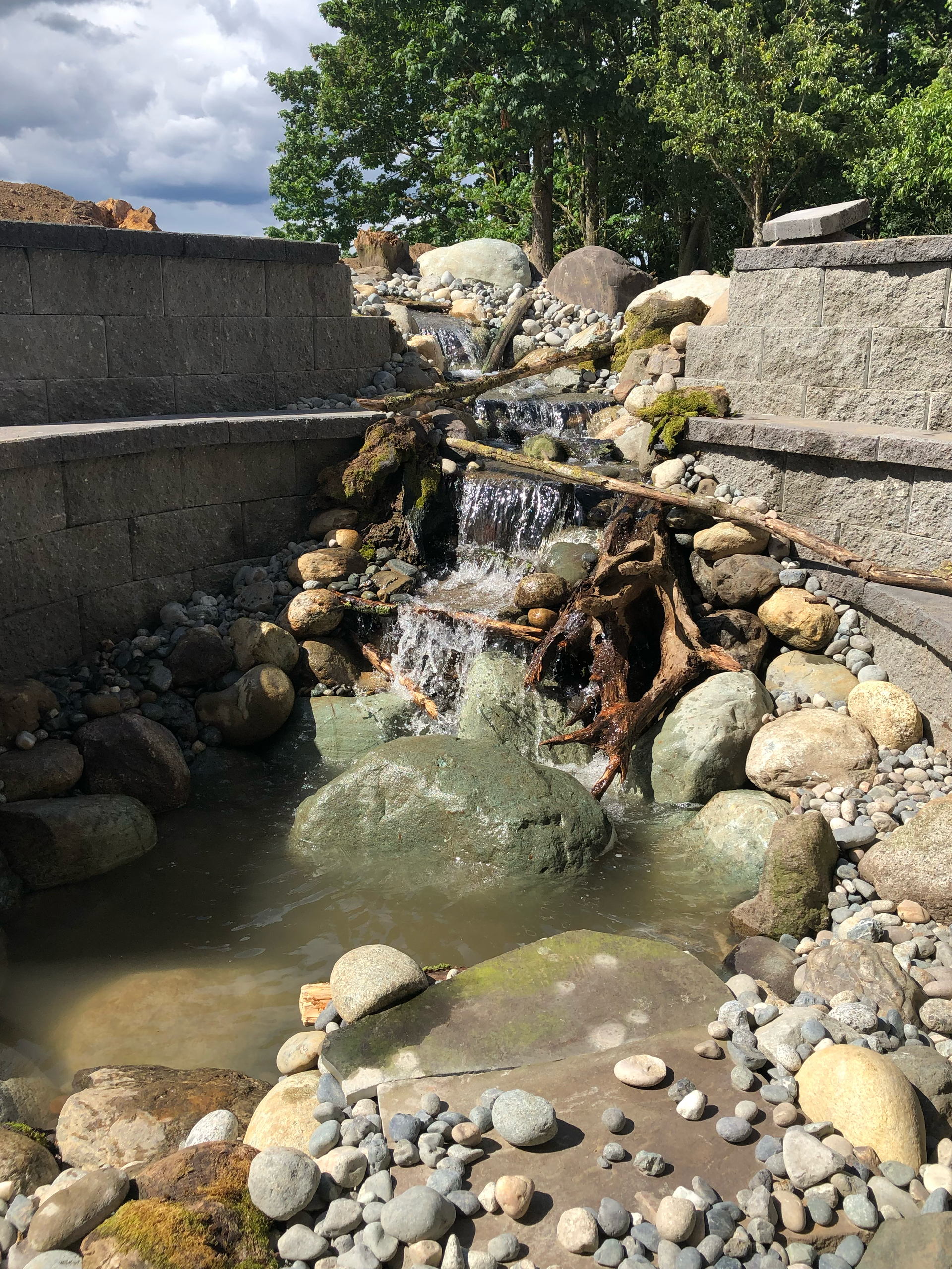 Water cascading down a rock and stone waterfall feature into a small pond; work by West Coast Landscape & Hardscape. 