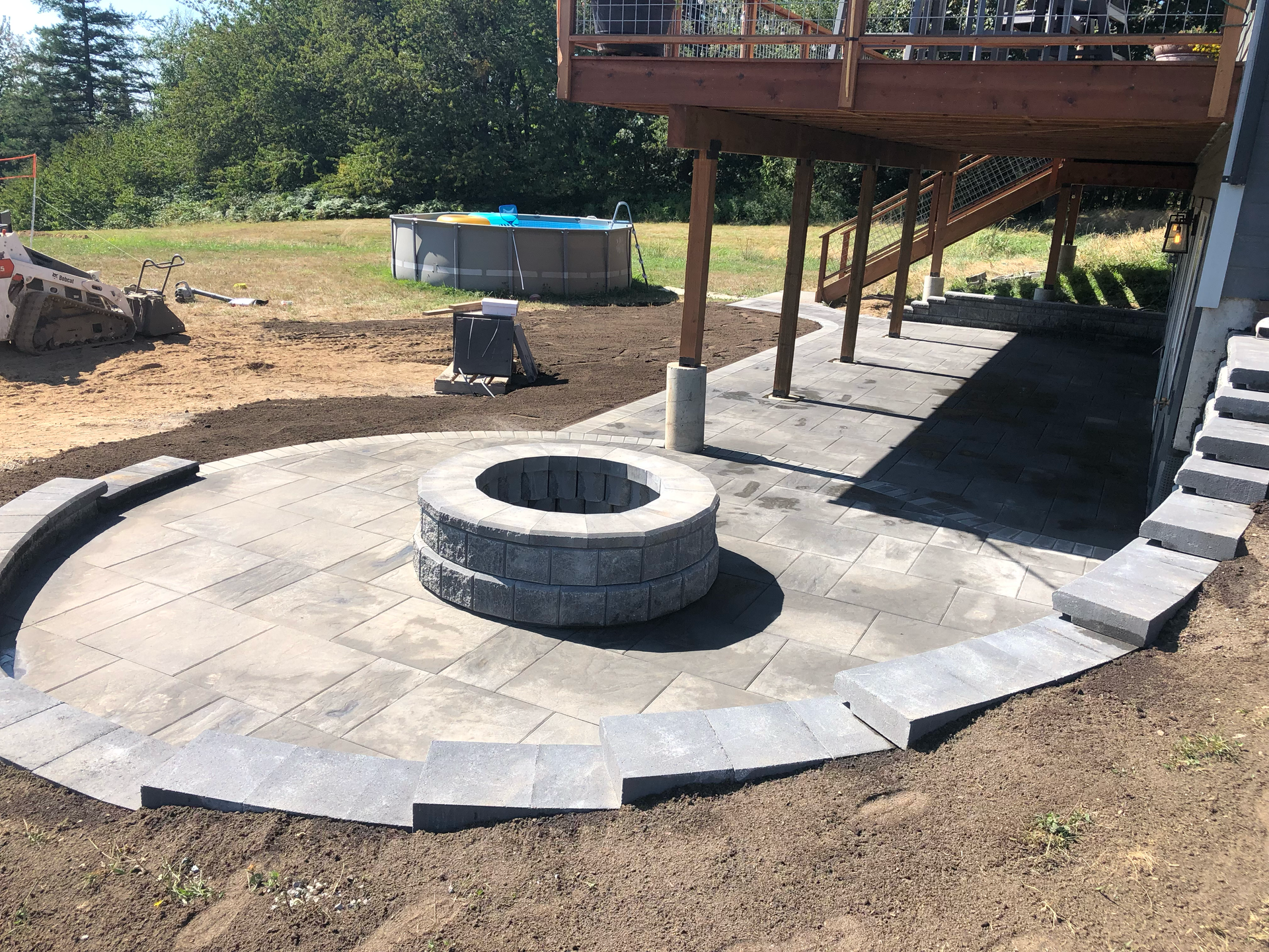 Circular patio with a fire pit, next to a deck and stairs; work by West Coast Landscape & Hardscape. 