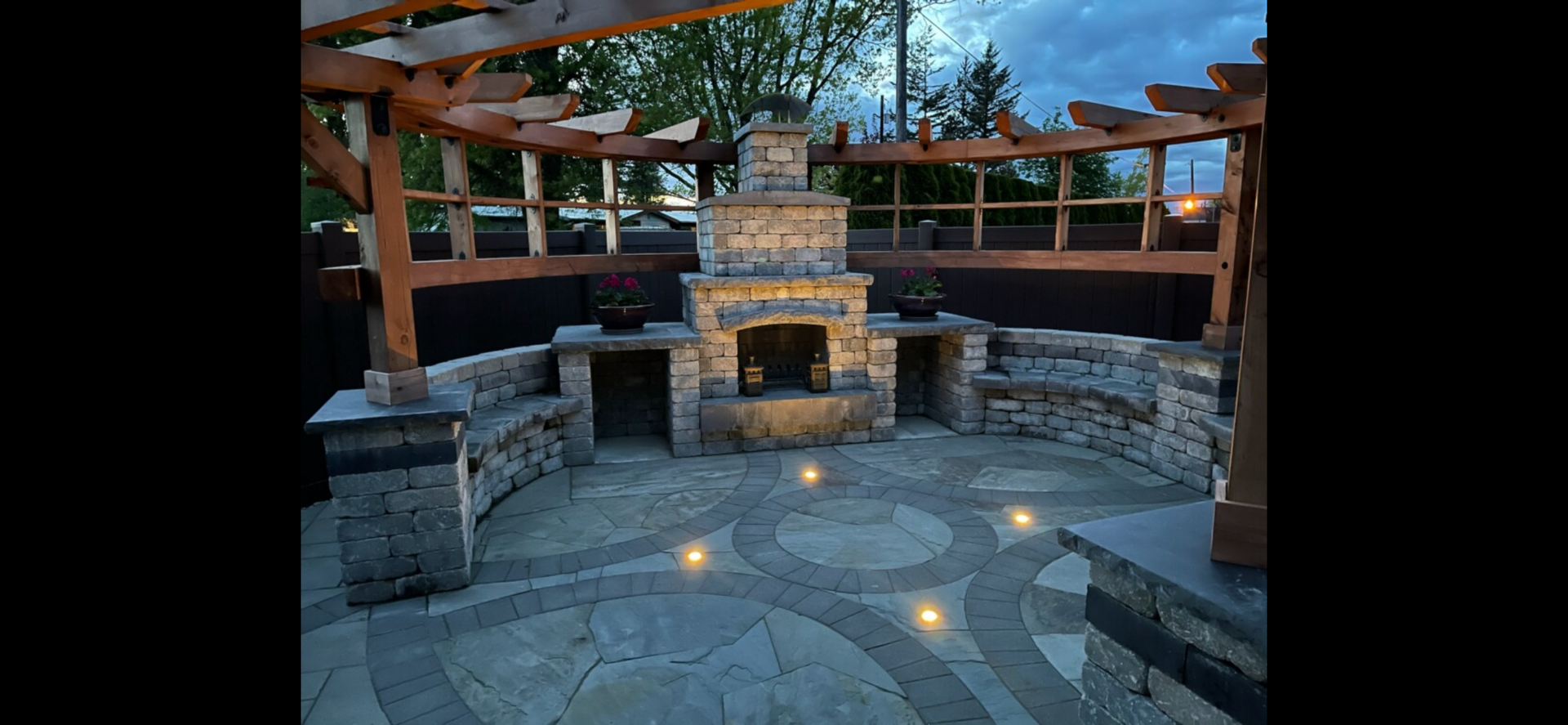 Outdoor stone patio with fireplace and pergola at dusk; work by West Coast Landscape & Hardscape. 