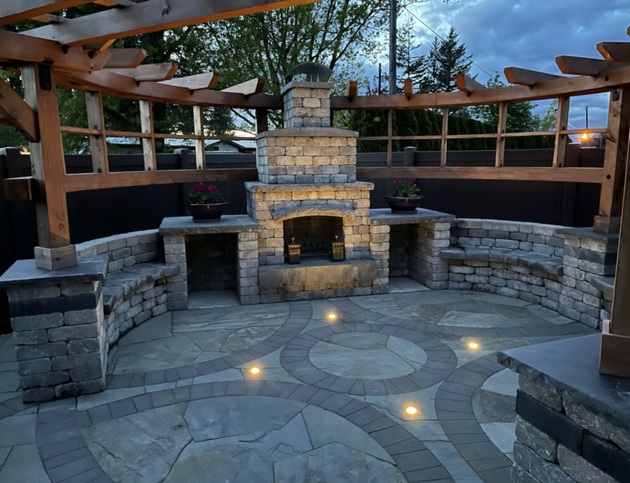 Stone patio with fireplace, built-in seating, and pergola at dusk; ; by West Coast Landscape & Hardscape. 