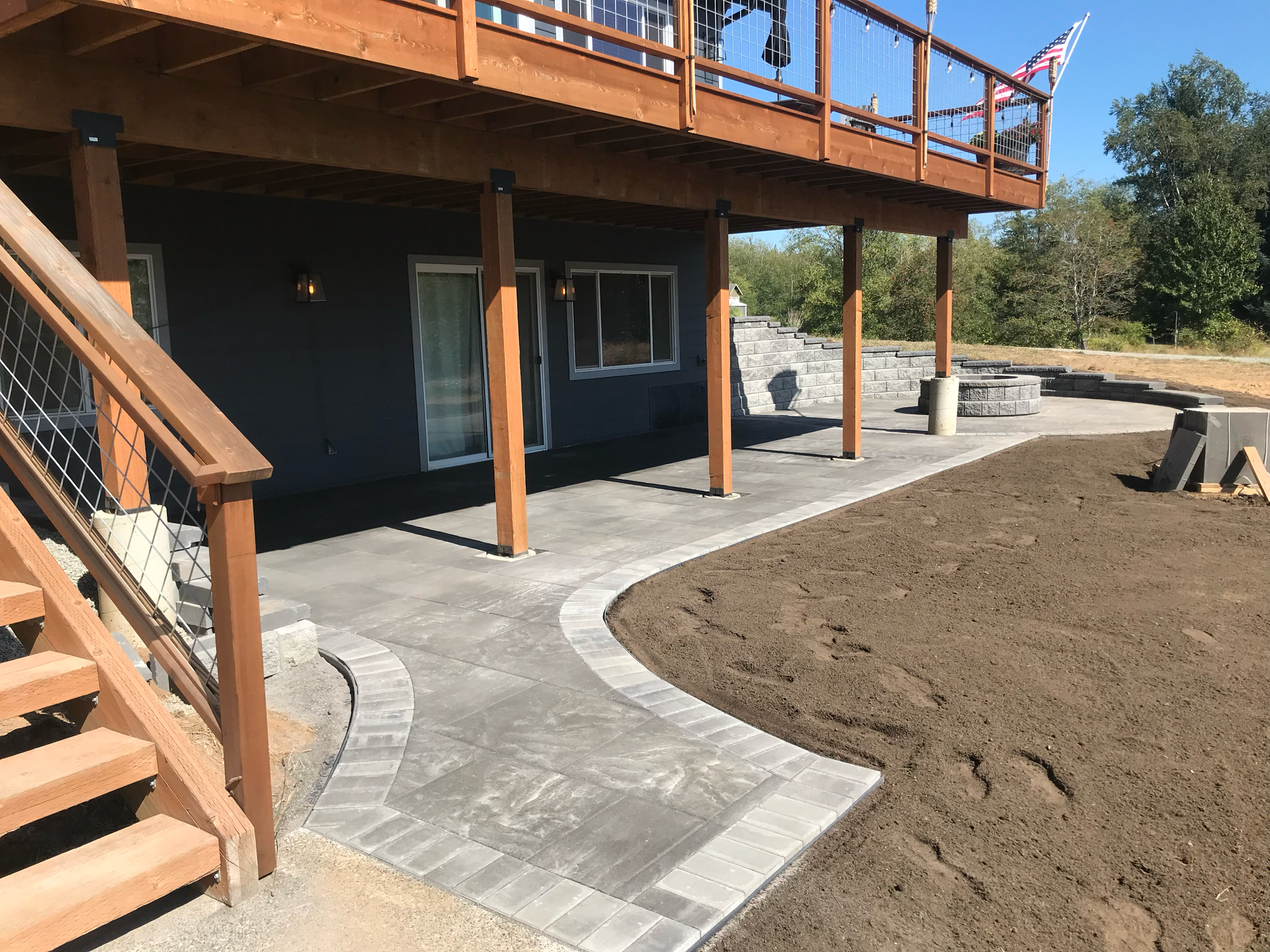 Exterior of a house with a wooden deck, concrete patio, and stairs, on a sunny day; work by West Coast Landscape & Hardscape. 