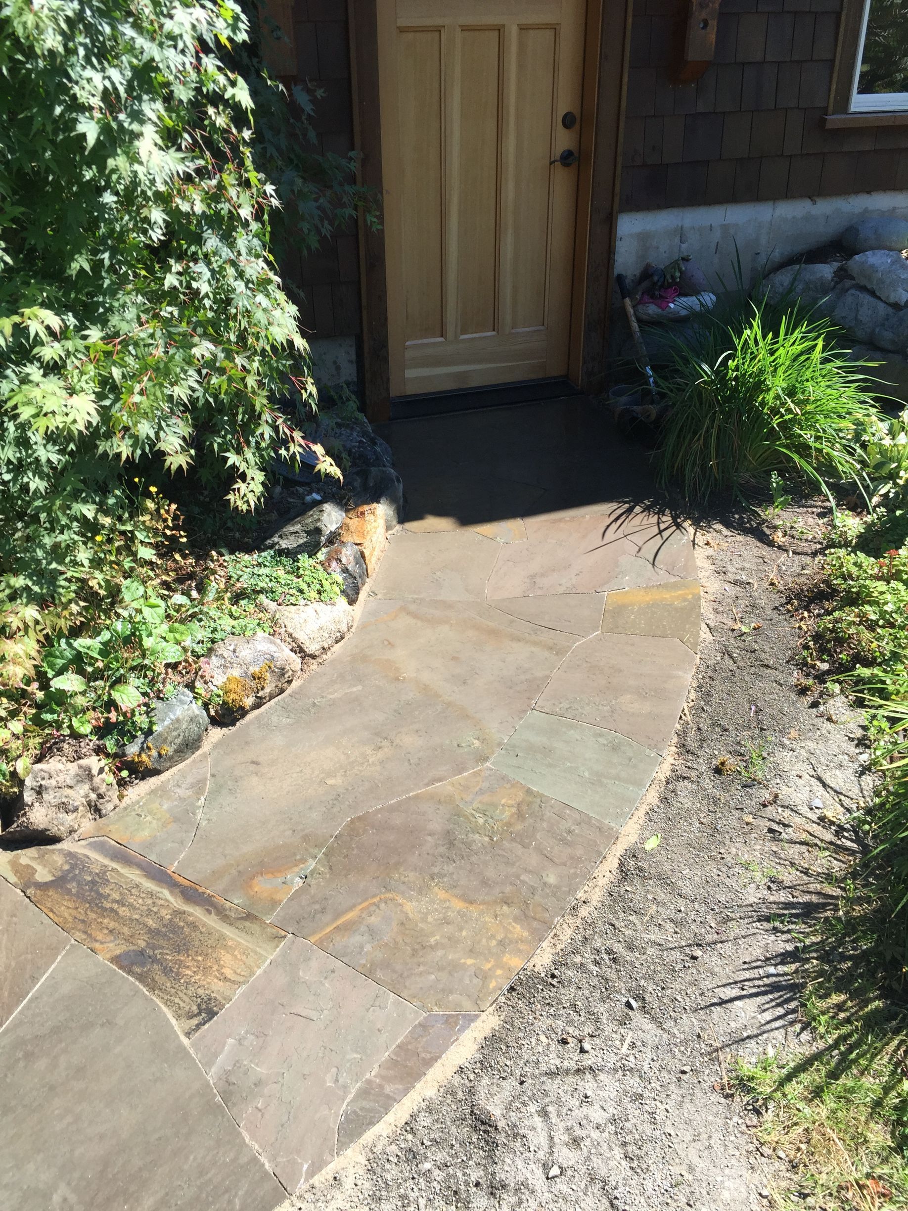 Stone path leads to a wooden door, surrounded by greenery and gravel; work by West Coast Landscape & Hardscape. 