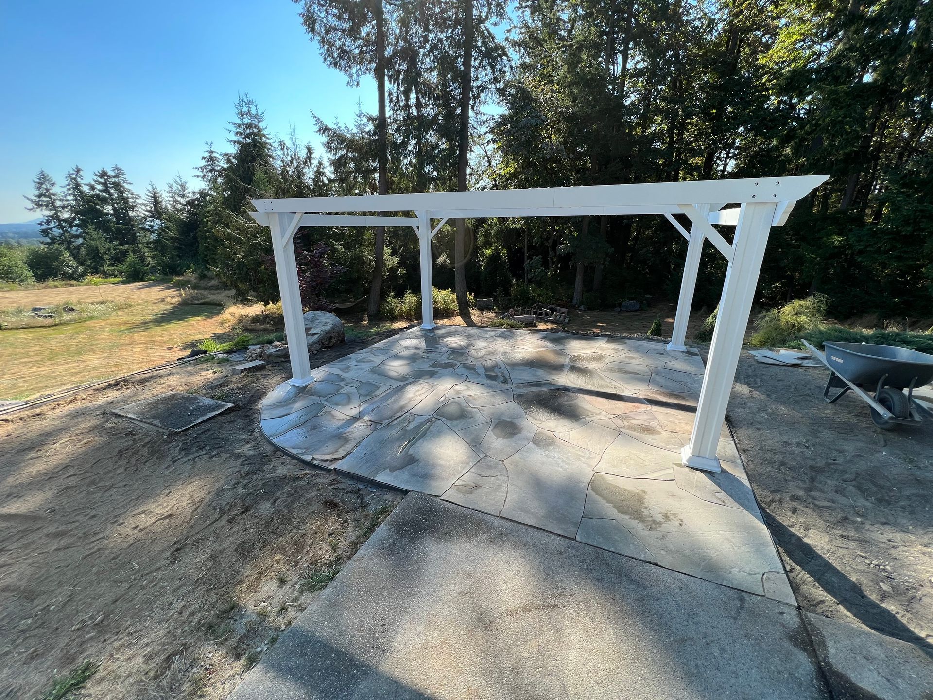 White outdoor pergola frame over concrete slab in a wooded yard under construction