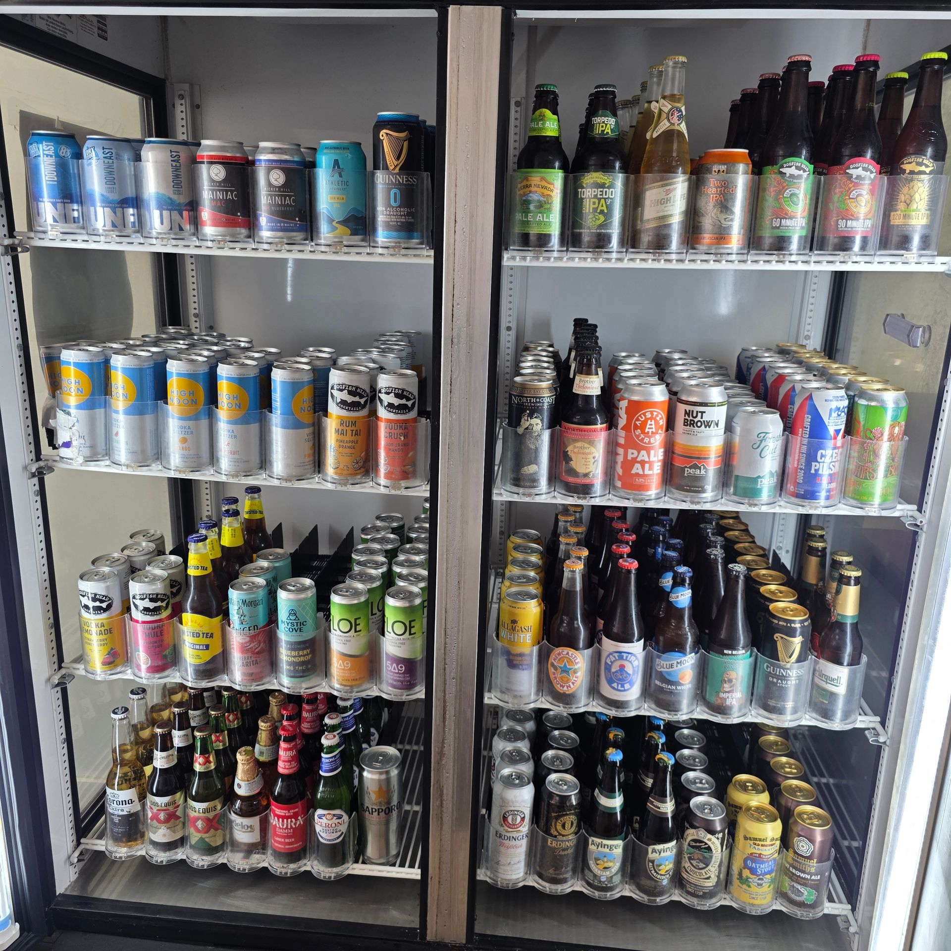 Refrigerated display with various beer cans and bottles, well organized in a store setting.