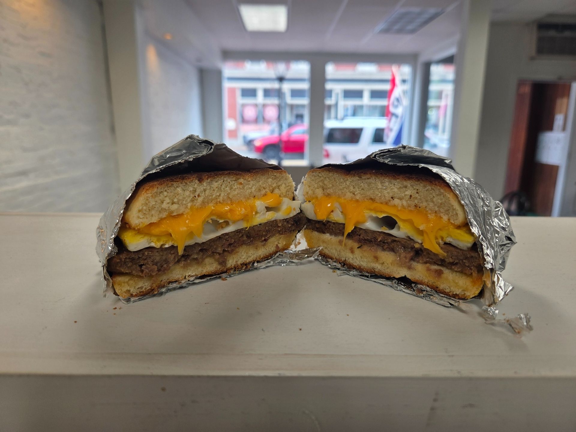 A wrapped sandwich cut in half. Visible: burger, egg, cheese, foil, interior shot.