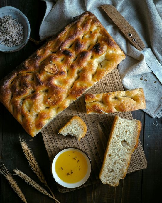 Focaccia bread with olive oil, salt, and knife on a rustic surface, close-up shot.