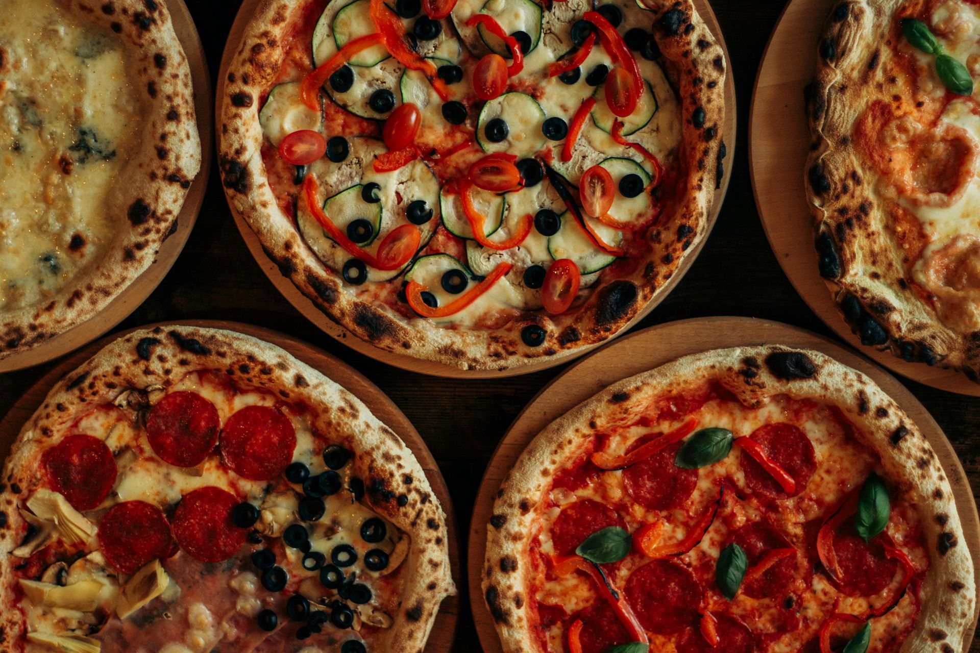 Several pizzas with various toppings: pepperoni, vegetables, and cheese, on wooden platters.