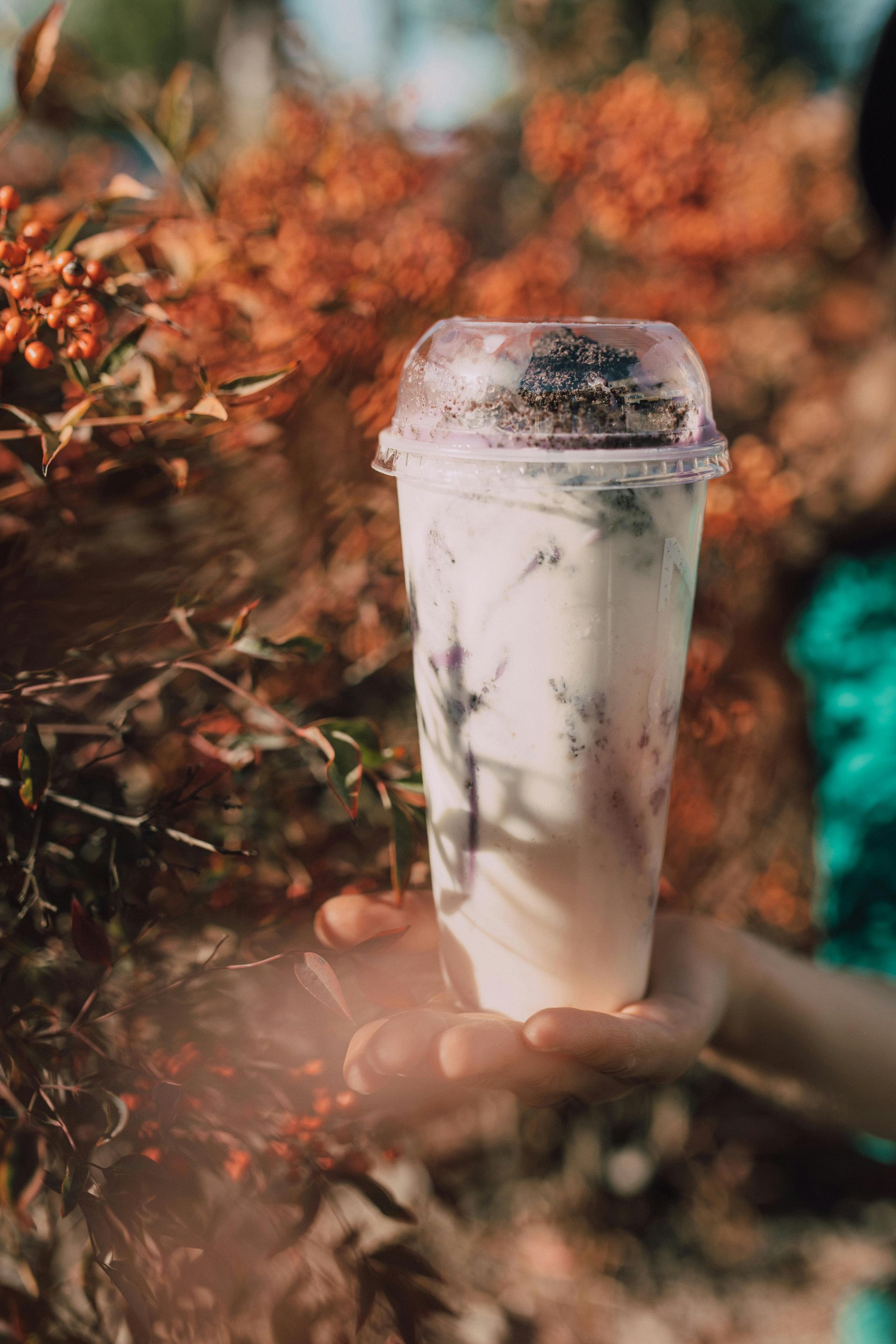 Person holding a clear plastic cup with a milky drink and dark pieces; orange berries in background.