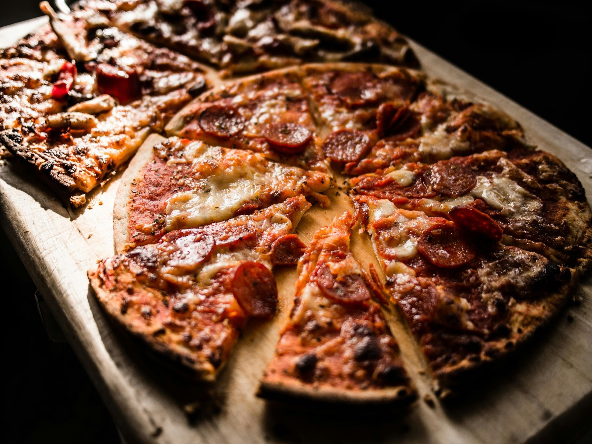Several pizzas on a wooden board, one with pepperoni and slices missing.