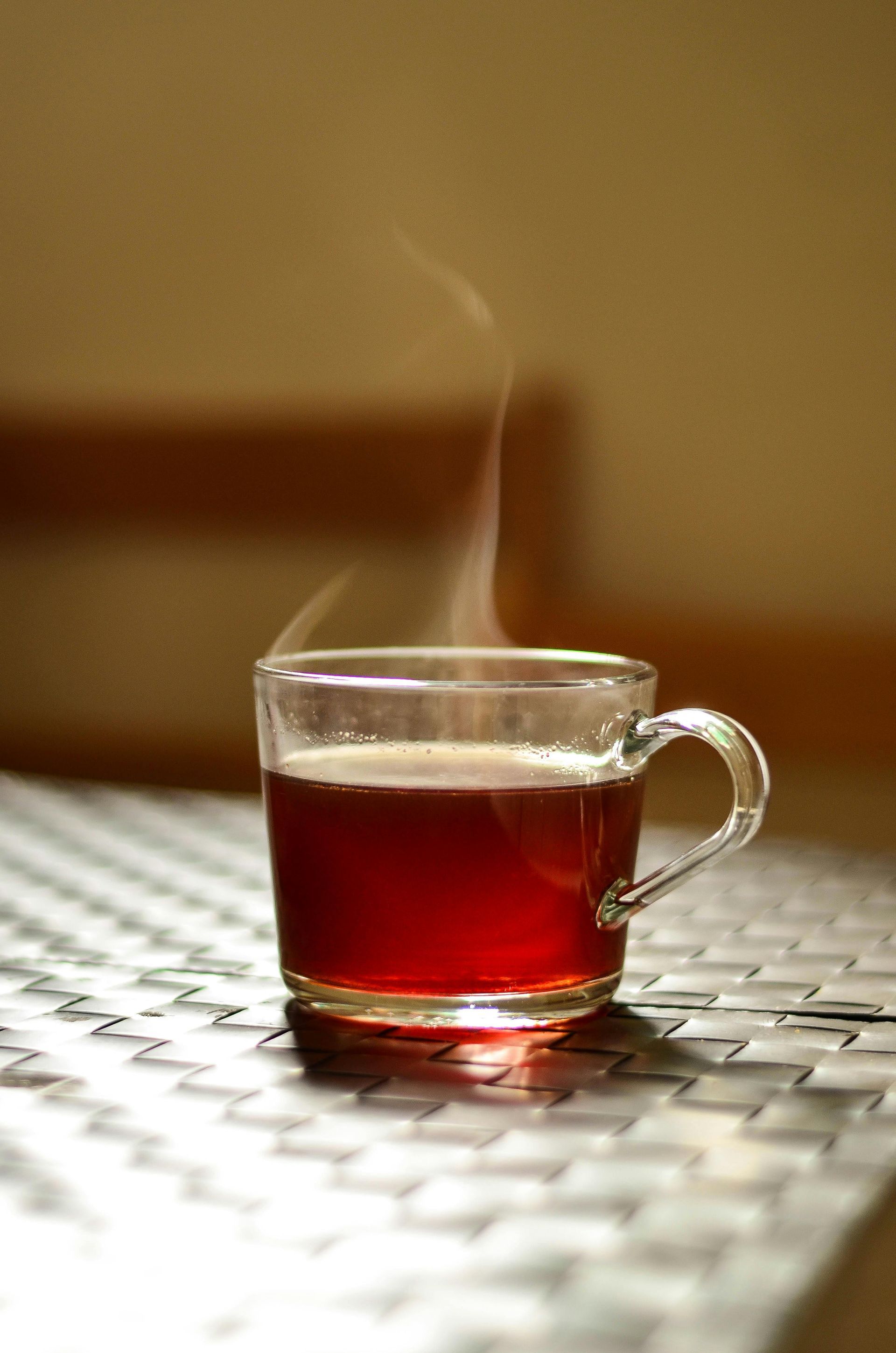 A clear glass mug filled with steaming red liquid, sitting on a textured surface.
