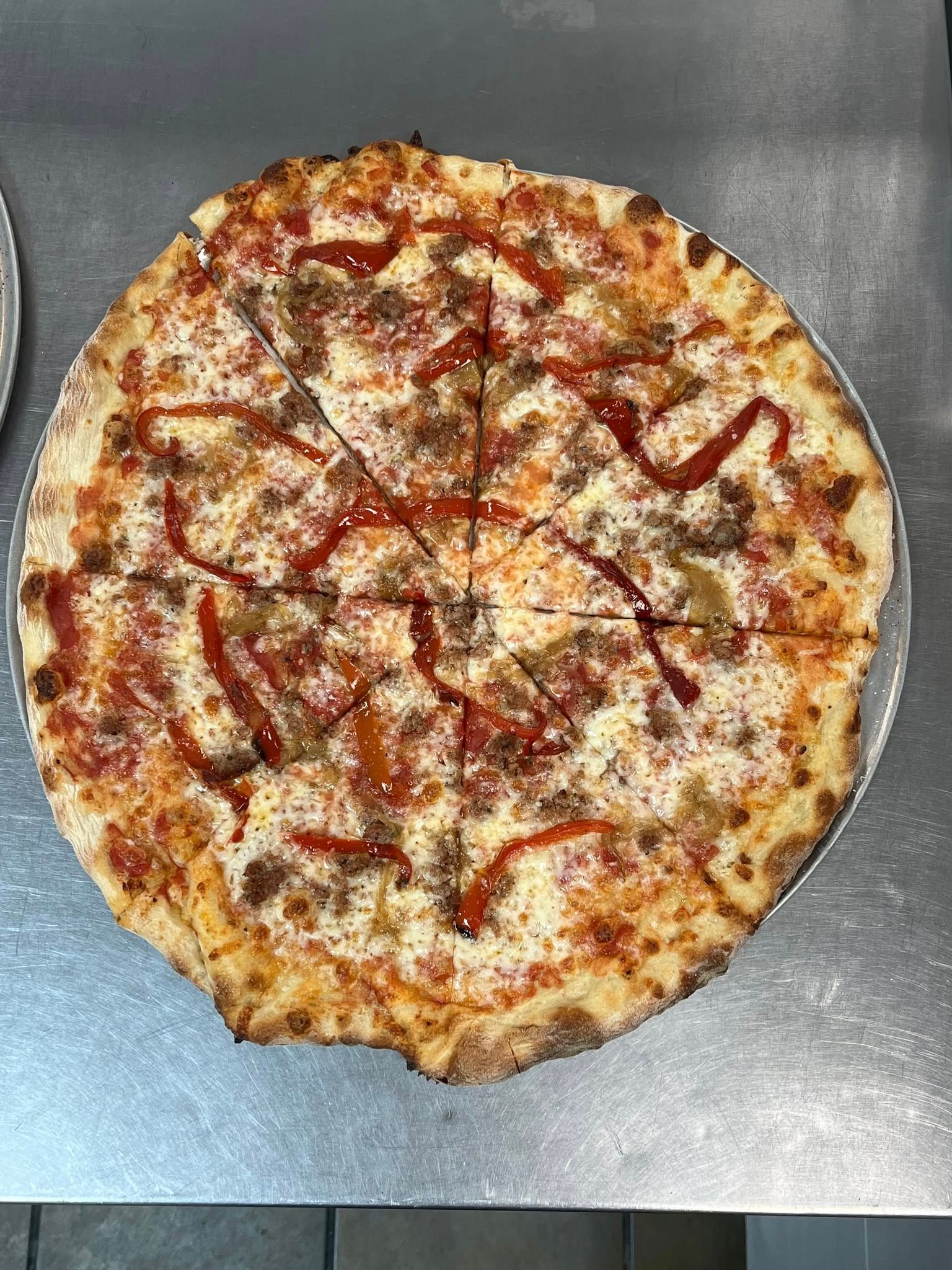 Pizza on a metal surface, sliced, with red sauce drizzled on top.