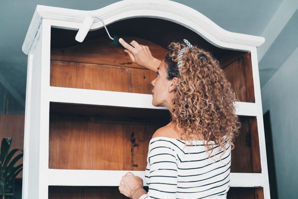 A woman is painting a wooden shelf with white paint.