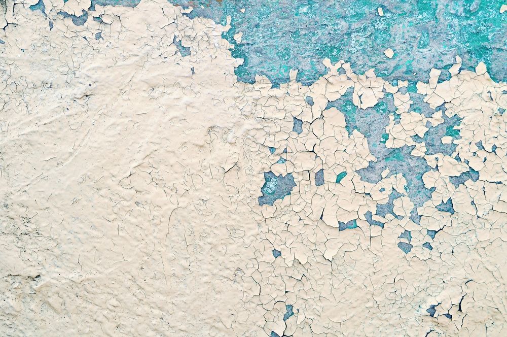 A close up of a white and blue wall with peeling paint.