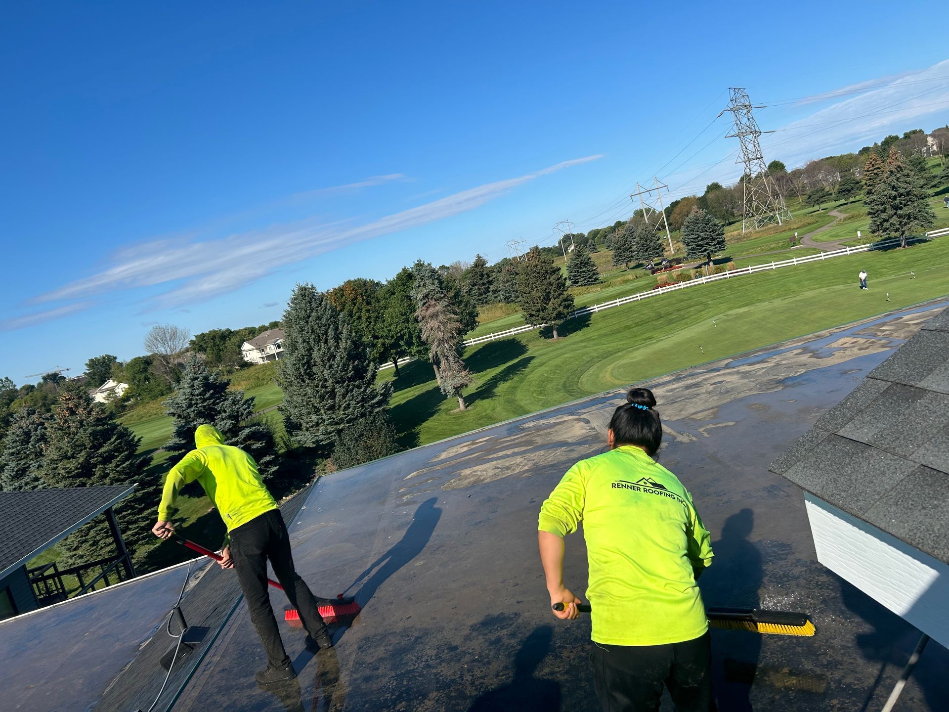 Two people are cleaning a roof with a golf course in the background.