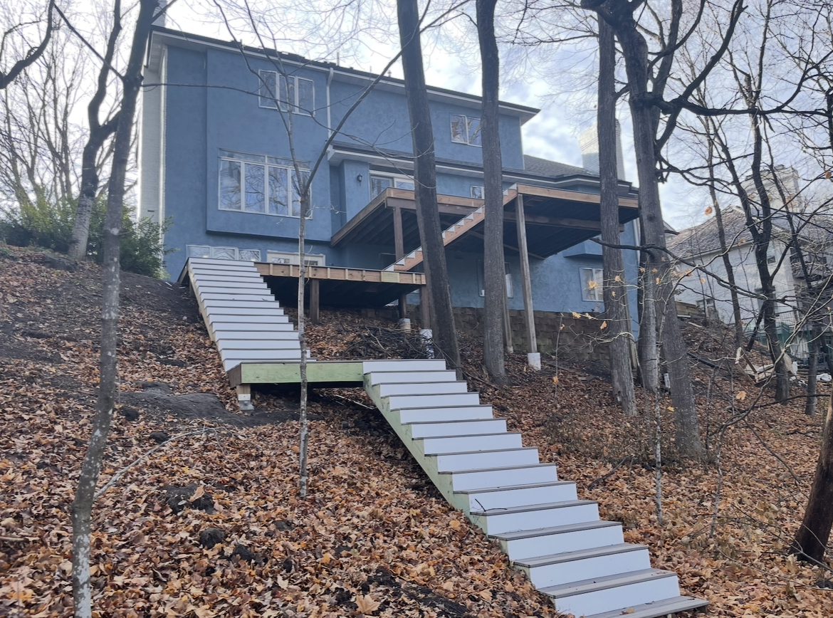 A blue house with stairs leading up to it is surrounded by trees and leaves.