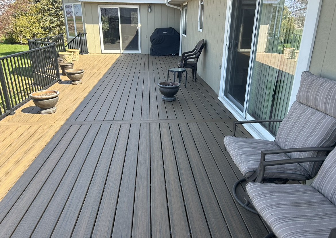 A large wooden deck with chairs and potted plants in front of a house.