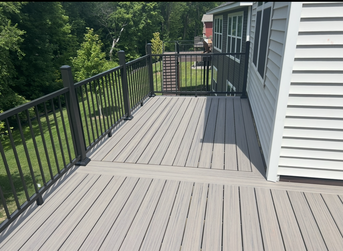 A large deck with a black railing and a white house in the background.