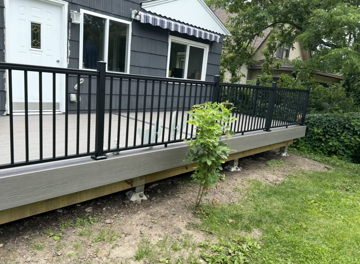A deck with a black railing is in front of a house.