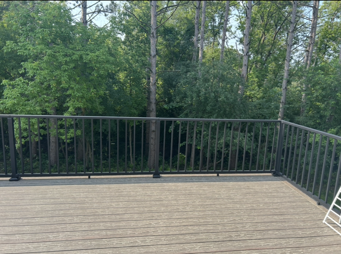 There is a deck with a railing and trees in the background.