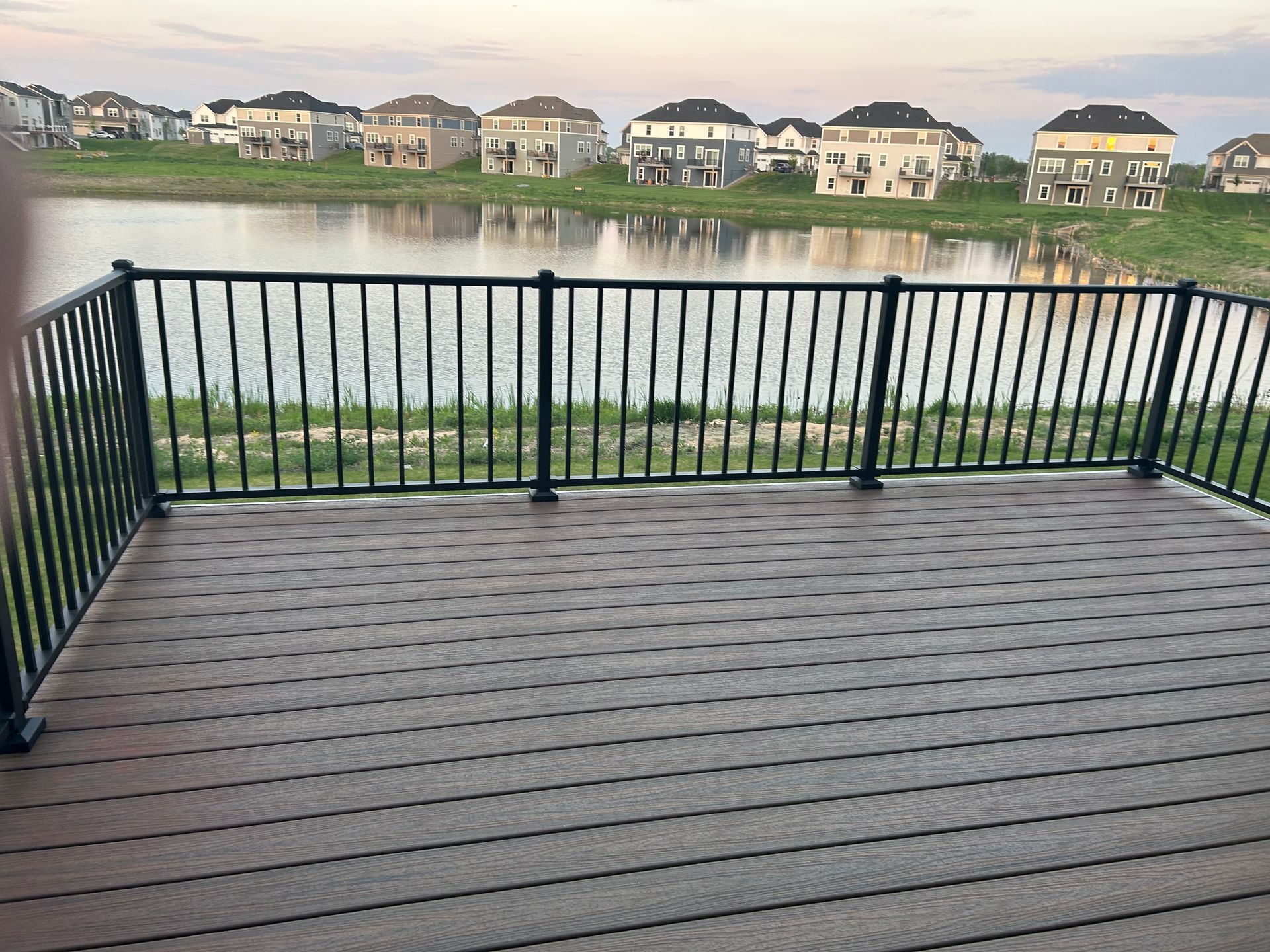 A deck with a railing overlooking a lake with houses in the background.
